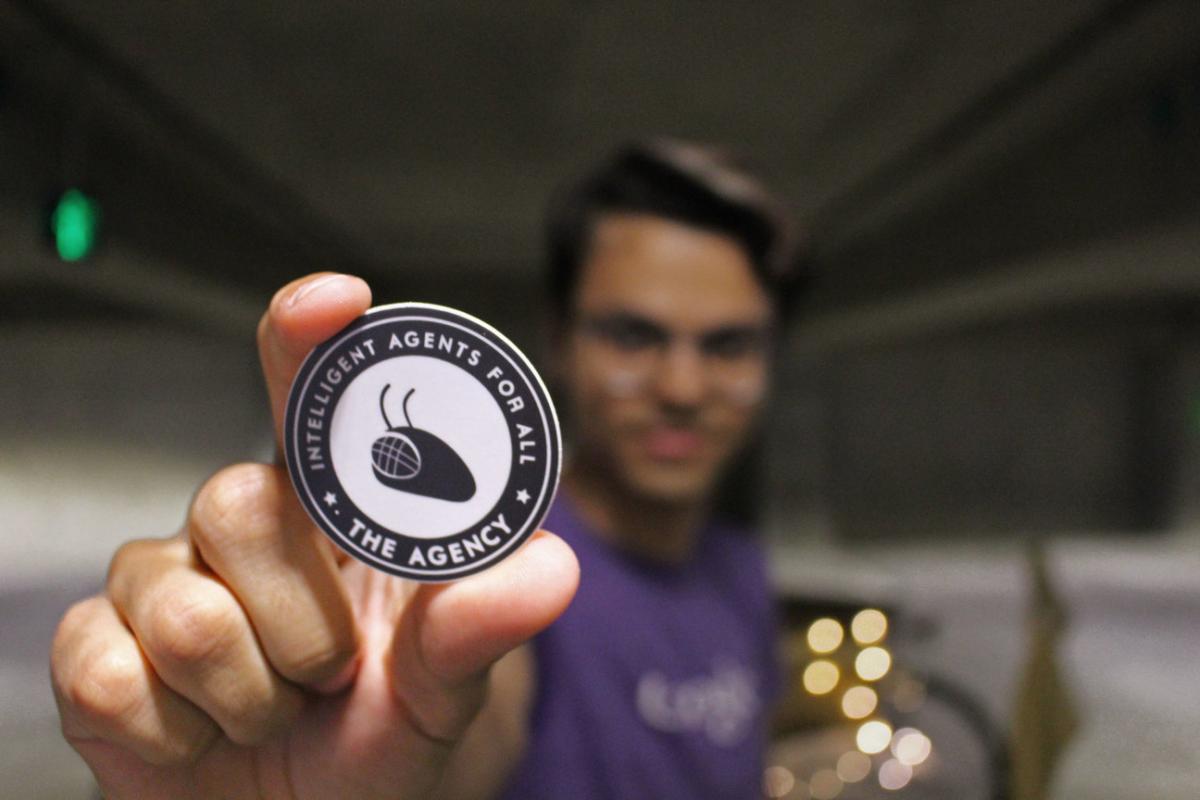 The Agency alum, Rapha Gontigo Lopes holds a button featuring the Agency's logo.